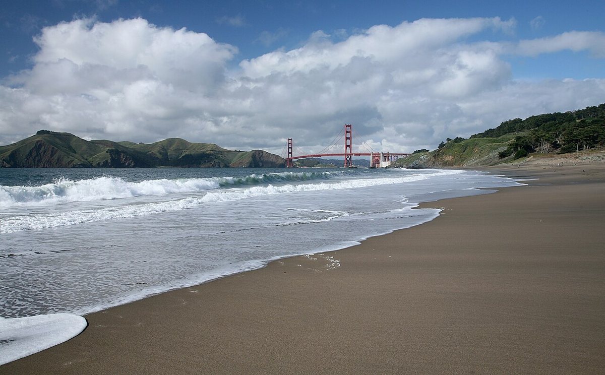 Couple sitting on the sand at Baker Beach with the Golden Gate Bridge rising behind them